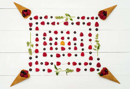 Top view of sweet fresh organic raspberries and blackcurrants in waffle cones. Frame of fresh berries in cones on white wooden background with blank space. Summer and healthy food concept の写真素材