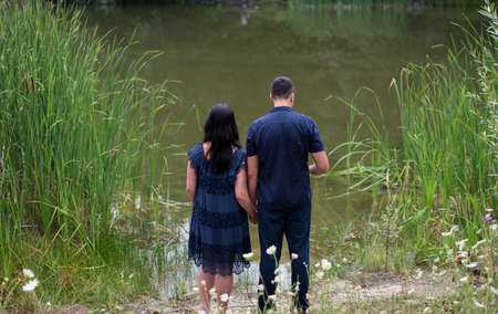 Couple in love walking and holding hands on the river bank outdoors, back view. Man and woman in blue clothing, free spaceの写真素材