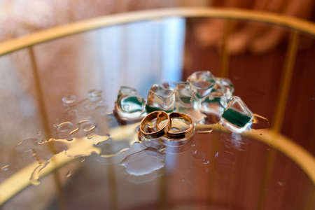 Golden wedding rings with  ice cubes on glass table with copy spaceの写真素材