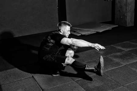 Muscular bearded man doing pistol squats on one leg in gym