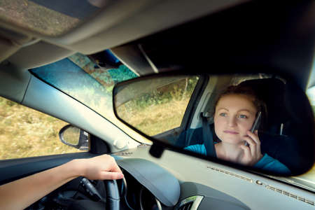 Reflection in the mirror of beautiful young woman driving a car and talking on smart phone, free...
