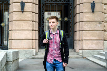 Portrait of stylish young man in plaid shirt and jacket with backpack walking in the city outdoors. Student travel, free spaceの写真素材