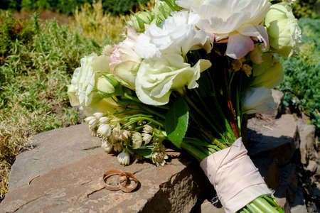 Two golden wedding rings on stone near   beautiful wedding bouquet of white and pink peony and roses in blur outdoors, selective focus, close upの写真素材