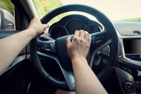 Close up of woman hand pressing the horn button while driving a car through the road. Woman driving a car with hand on horn button. Closeup woman hand holding steering wheel and honking the hornの写真素材