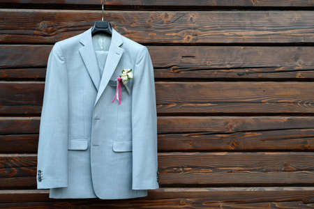 Stylish elegant wedding groom suit with boutonniere hanging on wooden background with copy space. Groom wedding accessories, free spaceの写真素材