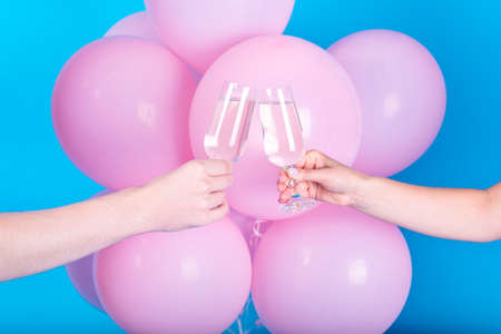 Man and woman clanging wine glasses with champagne with pink balloons on blue background, close up....
