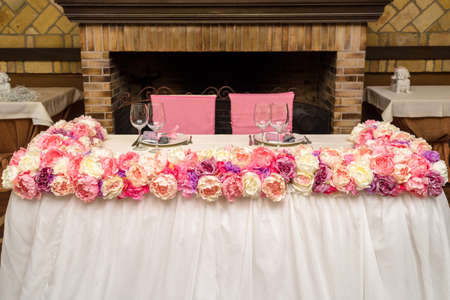 Beautiful pink and creamy flowers on table of newlyweds at wedding reception in restaurant, free space. Wedding table decorated with flowers, served for two peopleの写真素材