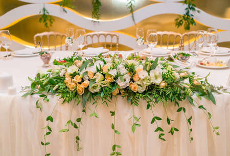 Lush floral arrangement of white and orange fresh flowers and greenery on wedding table for newlyweds. Beautiful flowers on table with white cloth, free space. Luxury wedding table decorationsの写真素材