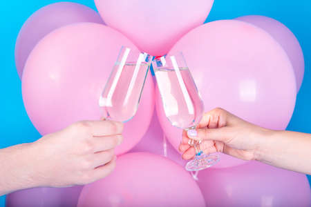 Man and woman clanging wine glasses with champagne with pink balloons on blue background, close up. Cheers. Man and woman hands toasting with champagne. Romantic momentの写真素材