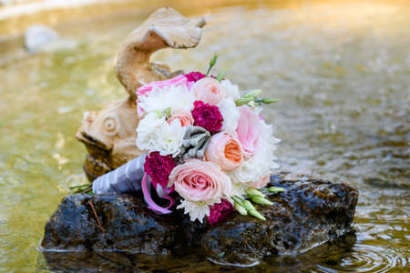 Close up of beautiful fresh wedding bouquet of pink and white roses on stone in water  near fish in fountain, free space. Wedding details outdoor with copy spaceの写真素材