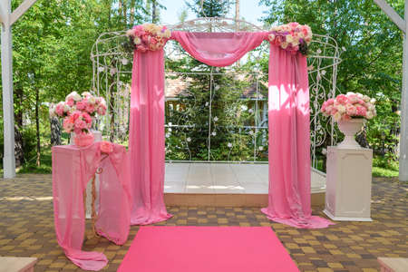 Place for wedding ceremony in pink color with wedding arch decorated with flowers and pink cloth outdoors. Beautiful wedding decorations with free spaceの写真素材