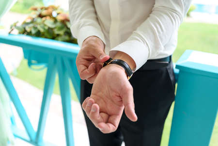 Close up of businessman putting on watch on his hand outdoors, free space. Man in white shirt with luxury wristwatches on hand. Groom wedding preparationの写真素材