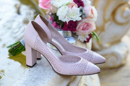 Beige bride shoes stand on stone fountain closeup near wedding bouquet and box with rings in blur. Wedding details outdoor with copy space. Wedding morning preparationの写真素材