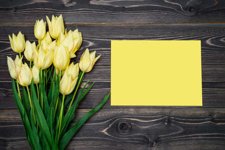 Spring background with yellow tulip flowers and yellow sheet of paper, copy space. Flat lay, top view, horizontal. Holiday greeting card for Valentine's Day, Woman's Day (March 8, Mother's Day, Easterの写真素材