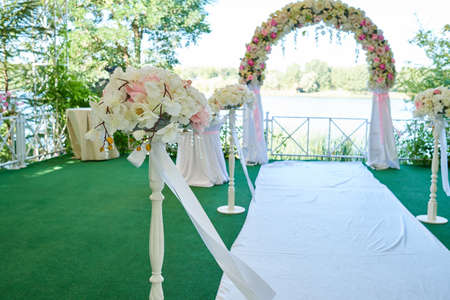 Beautiful wedding flowers with transparent fabric on archway, copy space. Wedding ceremony decorations outdoors. Stylish wedding arch in park near sea, lake or river in blurの写真素材