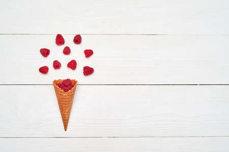 Ripe sweet raspberries in ice cream waffle cone, copy space. Fresh berries on white wooden background, free space. Summer and healthy food concept. Top view, flat lay. Berries background. Raspberries explosionの写真素材