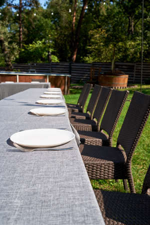 Empty ceramic round plates and cutlery on grey tablecloth on dinner table in garden outdoors, copy space. Dinner plate setting. White plate with knife and forkの写真素材