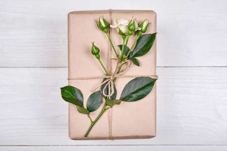 Top view of gift box with branch of fresh roses on wooden table, copy space. Holiday background, sale, shopping. Gift wrapping. Greeting card for Valentines Day, Womens Day, Mothers Day, flat layの写真素材