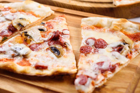 Slices of fresh homemade pizza with sausage, mushrooms, mozzarella and cheese on wooden board ready to eat, copy space. Italian traditional cuisine. Delicious italian food, shallow depth of fieldの写真素材