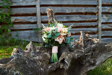 Beautiful wedding bouquet of fresh white and pink roses, blue flowers and greenery standing on wood stump outdoors, free space. Bridal bouquet, close upの写真素材