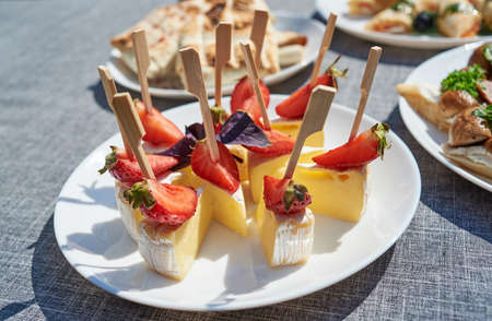 Canape with camembert cheese brie and strawberry on white plate, copy space. summer holiday reception outdoors. Buffet. Fruits and cheese on plateの写真素材