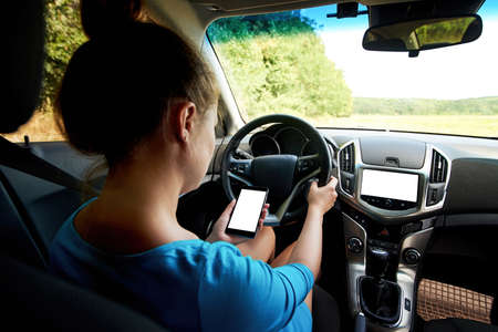 Back view of beautiful young woman driving a car (or standing in traffic congestion) and using mobile smart phone, free space. Business woman sitting in car with cellphoneの写真素材