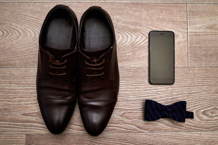 Close up of brown leather men shoes, blue bow tie and mobile phone on wood background, free space....