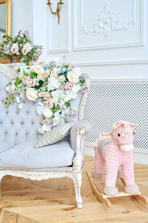 Soft sofa with gray fabric upholstery, pillows and flowers on it, copy space. Luxury rich living room interior design with elegant classic furniture, rocking horse and mirror. Vintage textile couchの写真素材