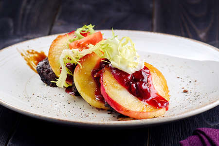 Grilled goose liver (foie gras) with sweet berry sauce and caramelized apples in white plate on table, free space. French cuisine, delicatessen restaurant meal, close upの写真素材