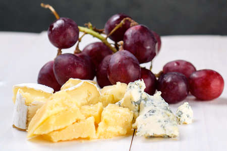 Delicious cheese and grapes on white wooden table, soft focuse. Camembert cheese, blue cheese, close up. Piece of cheese on white backgroundの写真素材