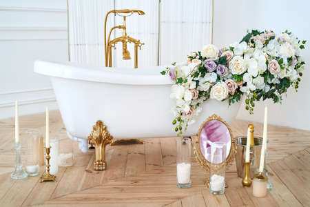 Beautiful luxury vintage empty bathtub with lush floral decorations and candles, mirror on the floor in bathroom interio, copy space. Freestanding white bath with flowers near folding screen. Romantic eveningの写真素材