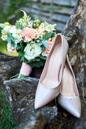 Close up of beautiful beige shiny bride shoes and wedding bouquet of pink and white roses in blur outdoors, soft focuse. Wedding morning preparation. Wedding bride accessories. Bridal bouquet and shoesの写真素材