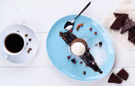 Tasty chocolate lava cake with vanilla ice cream ball and berries on plate on white table. Chocolate fondant with cup of coffee. Hot chocolate pudding. Top view, flat layの写真素材