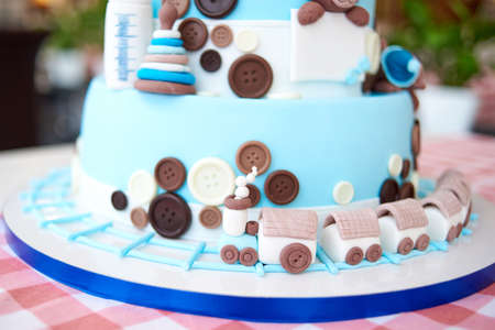 Close up of locomotive on round multi tiered blue  birthday cake decorated with button and toys on checkered tablecloth, copy space for textの写真素材