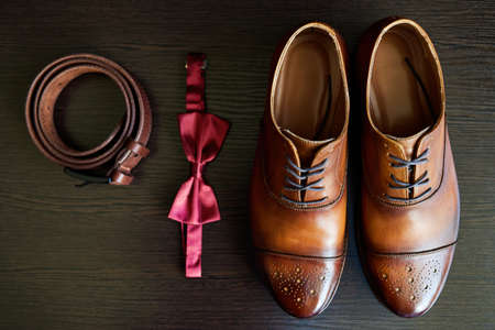 Close up of brown leather male shoes, bow tie and belt on wooden background. Modern man or groom accessories. Wedding details. Male casual outfits. Top view, flat layの写真素材
