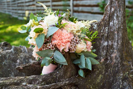 Beautiful wedding bouquet of fresh white and pink roses, blue flowers and greenery standing on wood stump outdoors, free space. Bridal bouquet, close upの写真素材