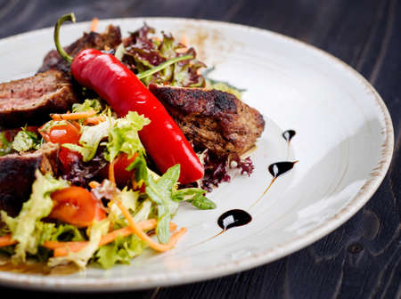 Veal salad with lettuce, carrot, tomato and pepper on white plate on dark wooden background, copy space. Restaurant food, close up. Meat saladの写真素材