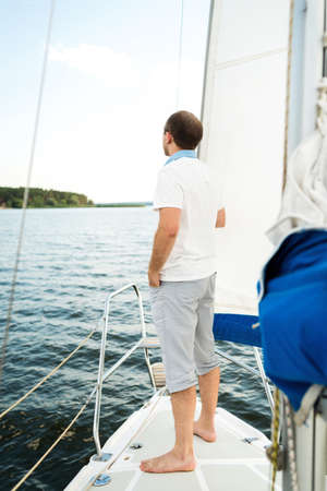 Handsome young man standing alone on yacht or sailboat in sea, copy space. Sailing, tourism, travel and people conceptの写真素材