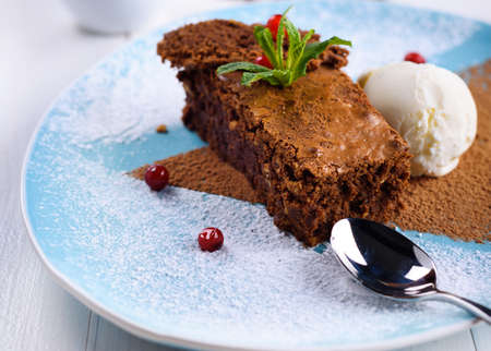 Tasty chocolate cake with ice cream, mint and berries on plate on the table on light background, close-up. Chocolate brownieの写真素材