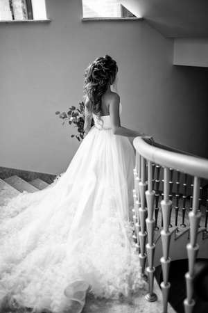 Full length body portrait of beautiful bride wearing fashion wedding dress with feathers walking down the stairs, back view. Black and white photoの写真素材
