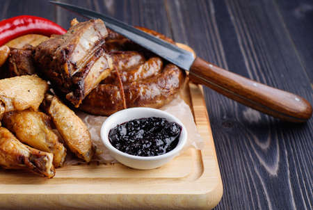 Mixed fresh grilled meat and sausage with pepper, french fries and sauce on wooden cutting board. Assorted meat with vegetables from summer BBQ. Healthy eating. Delicious barbecued ribsの写真素材