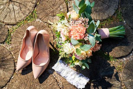 Top view of beige bride shoes, wedding bouquet and garter on wood background outdoors, copy space.の写真素材