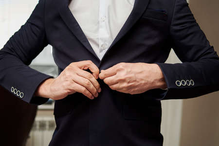 Man in white shirt and suit button his jacket indoors, close-up.の写真素材