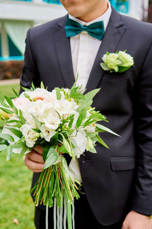 Bridal wedding bouquet of white flowers and greenery with ribbons in groom hand.の写真素材