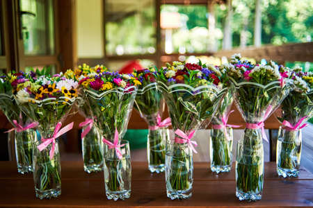 Many beautiful bouquets of bright wildflowers in  transparent glasses on wooden table, copy space.の写真素材