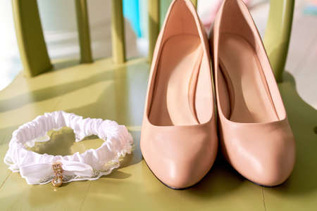 Beige leather bride's shoes and lace garter on chair, copy space.の写真素材