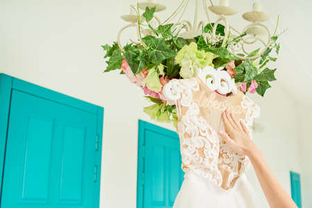 Bride touching by hand her wedding dress hanging on hanger with inscription in Russian ''Bride'' on chandelier with flowers on hotel terrace.の写真素材