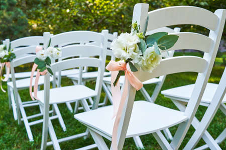 White fresh flowers with pink ribbon on wedding chair on each side of archway outroods; copy space....