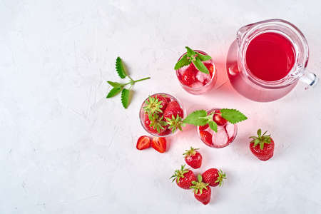 Strawberry lemonade, cocktail with ice and mint in glasses and jug on white concrete background, copy space.の写真素材