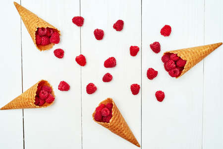 Ripe sweet raspberries in ice cream waffle cone, copy space. Fresh berries on white wooden...